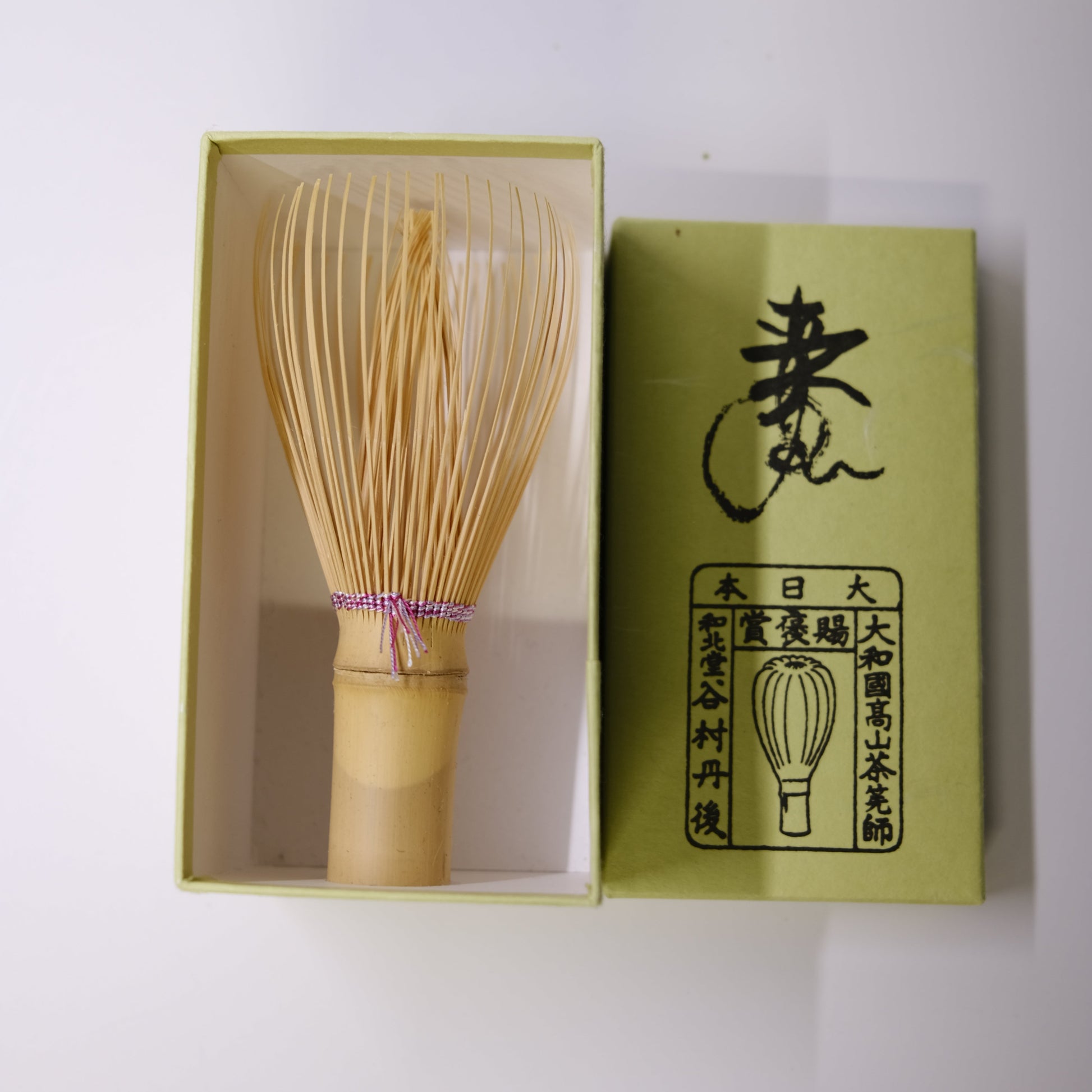 Wooden whisk in a green box with branding on a white background